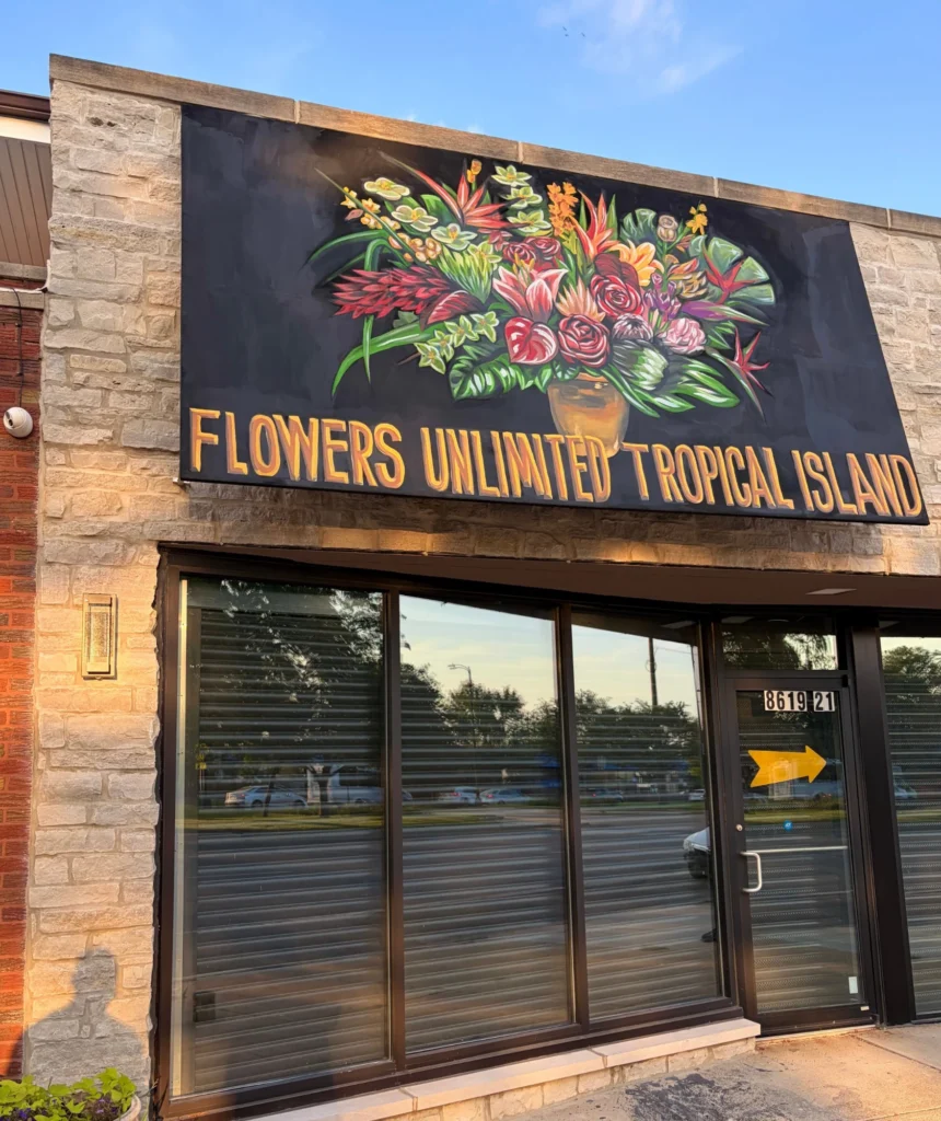 Flowers Unlimited Tropical Island Storefront, hand-painted sign by Caleb Wassell: a black sign with a vase of tropical flowers and gold lettering installed above the shop windows of a Chicago florist.