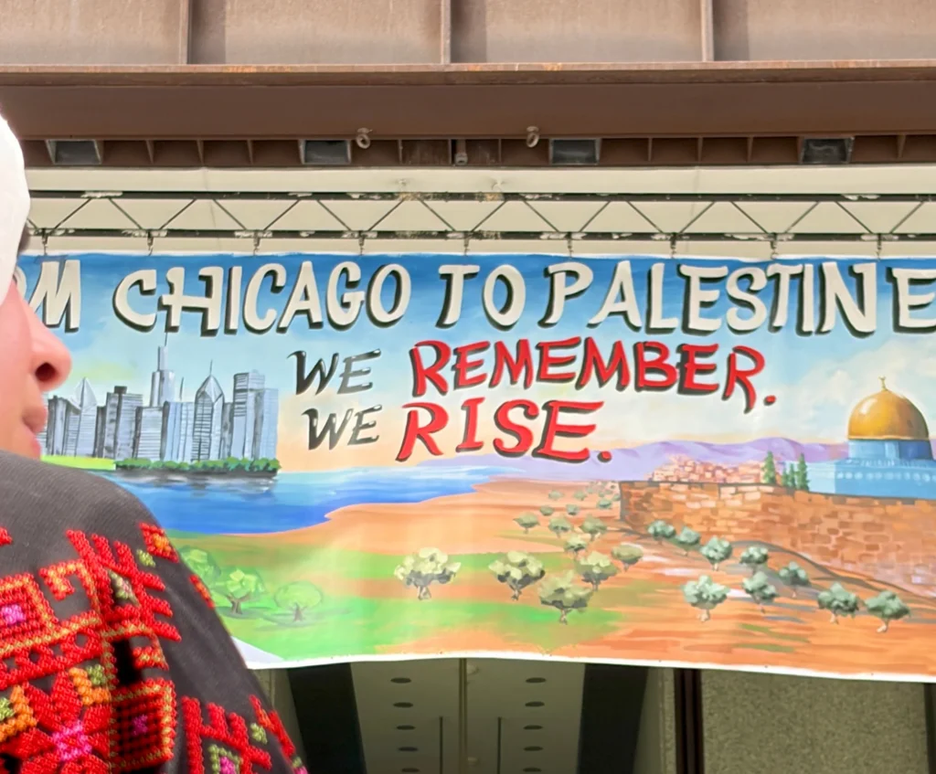 From Chicago to Palestine, detail of the banner by Caleb Wassell: the words We Remember. We Rise. between the Chicago skyline and the Dome of the Rock, seen behind a woman in an embroidered thobe.