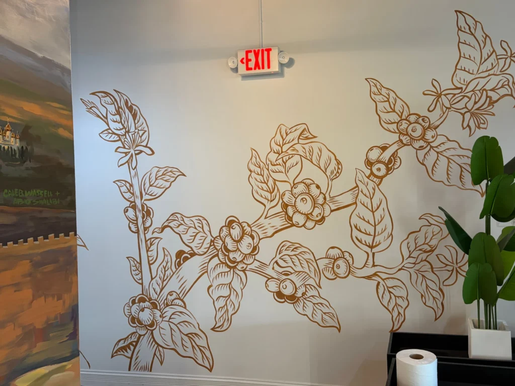 Coffee Branches, theQahwa, mural by Caleb Wassell: a line drawing of coffee branches with cherries, leaves and blossoms painted in copper on a white cafe wall.